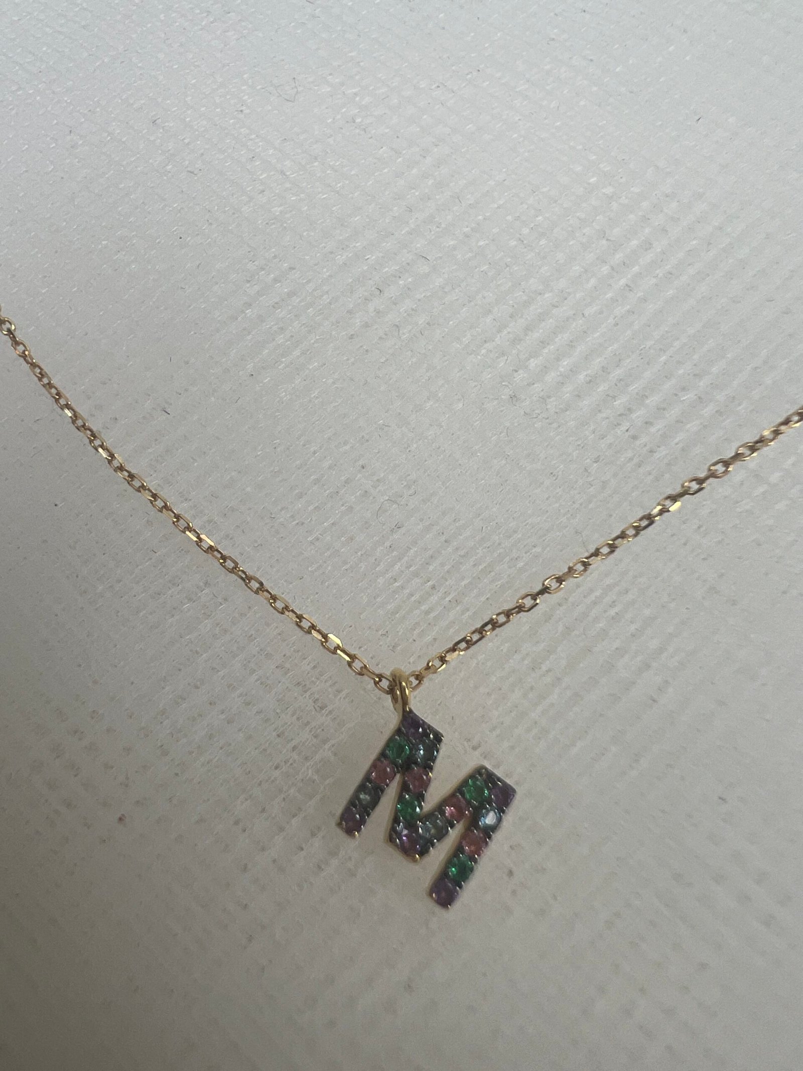 Cadena de oro amarillo con inicial de zafiros de colores.
