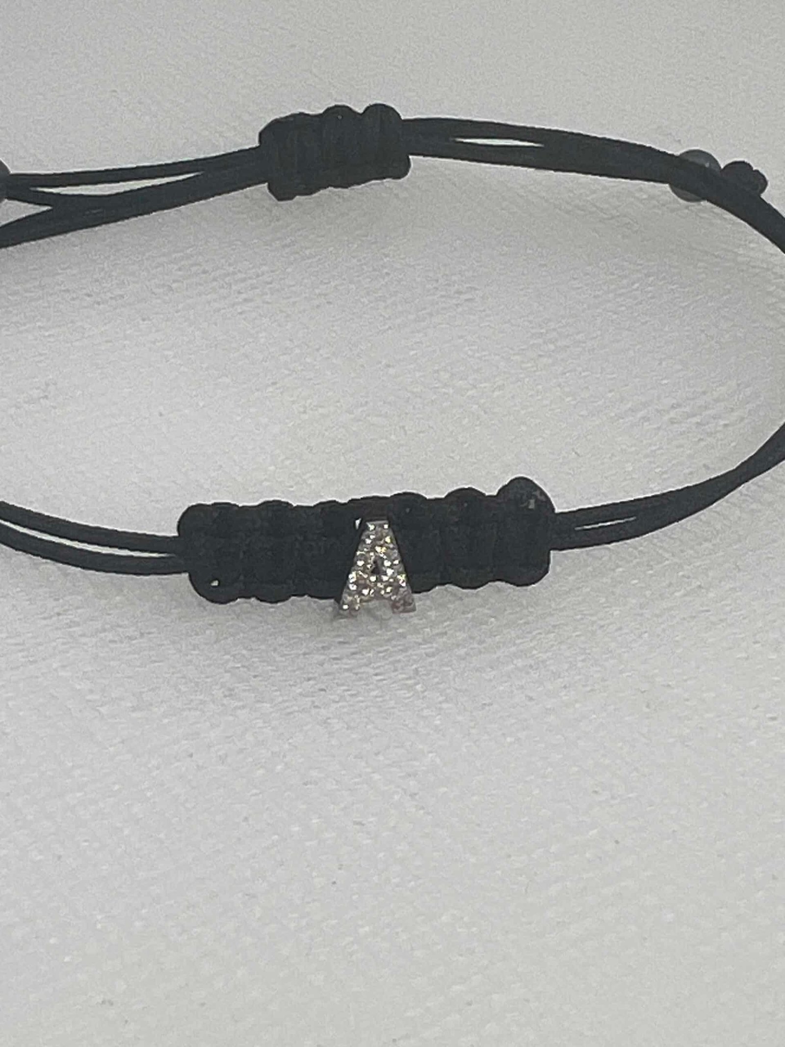 Pulsera de macrame de color negro con inicial de oro blanco y brillantes.
