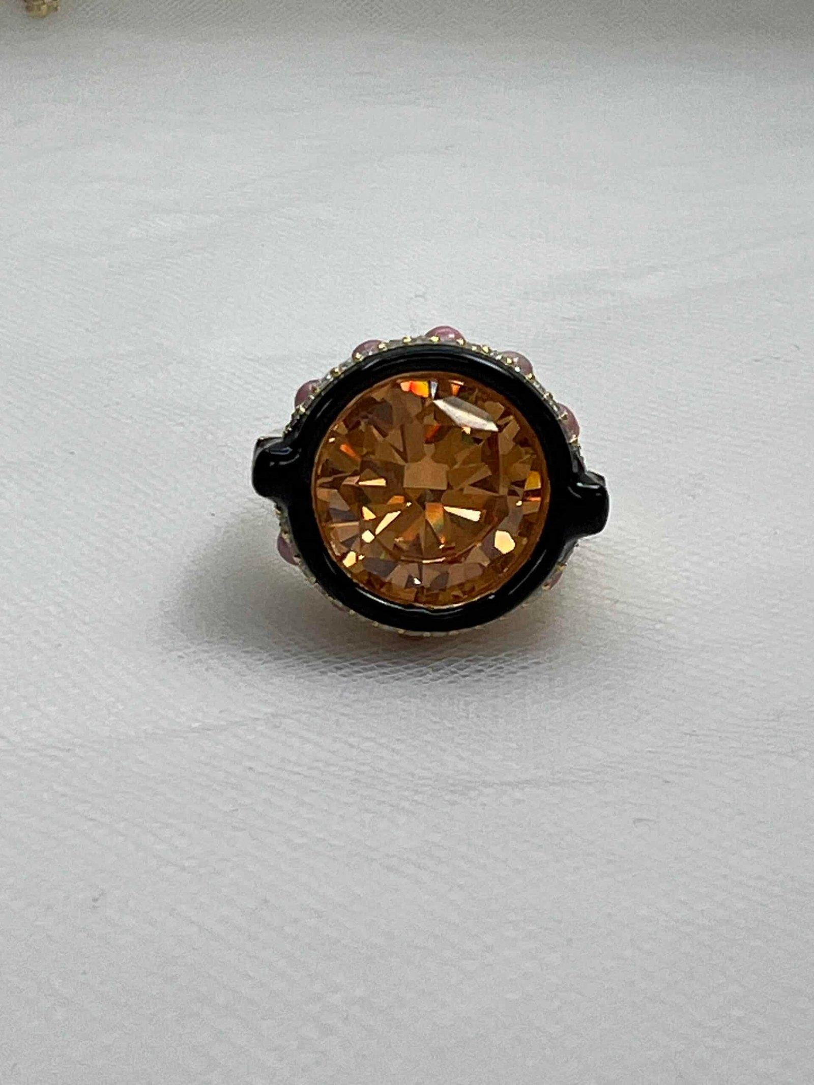 Anillo de plata chapado en oro amarillo con circonita de color ambar bordeada de esmalte negro y piedras naturales y circonitas blancas.