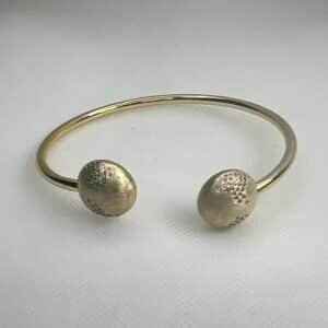 Esclava de plata chapada en oro amarillo abierta en el centro con medias bolas matizadas y circonitas engastadas de distinto tamaño.