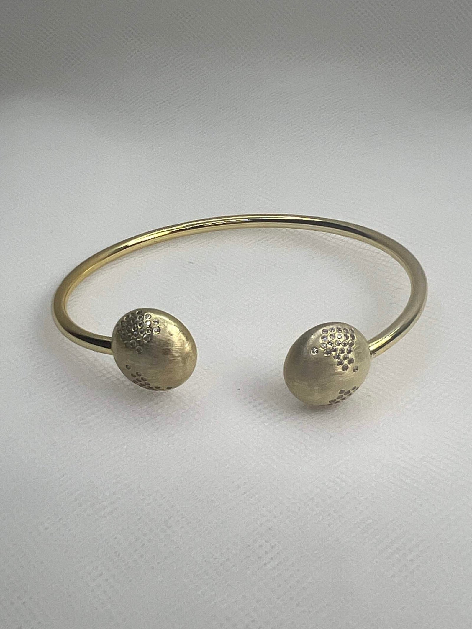 Esclava de plata chapada en oro amarillo abierta en el centro con medias bolas matizadas y circonitas engastadas de distinto tamaño.